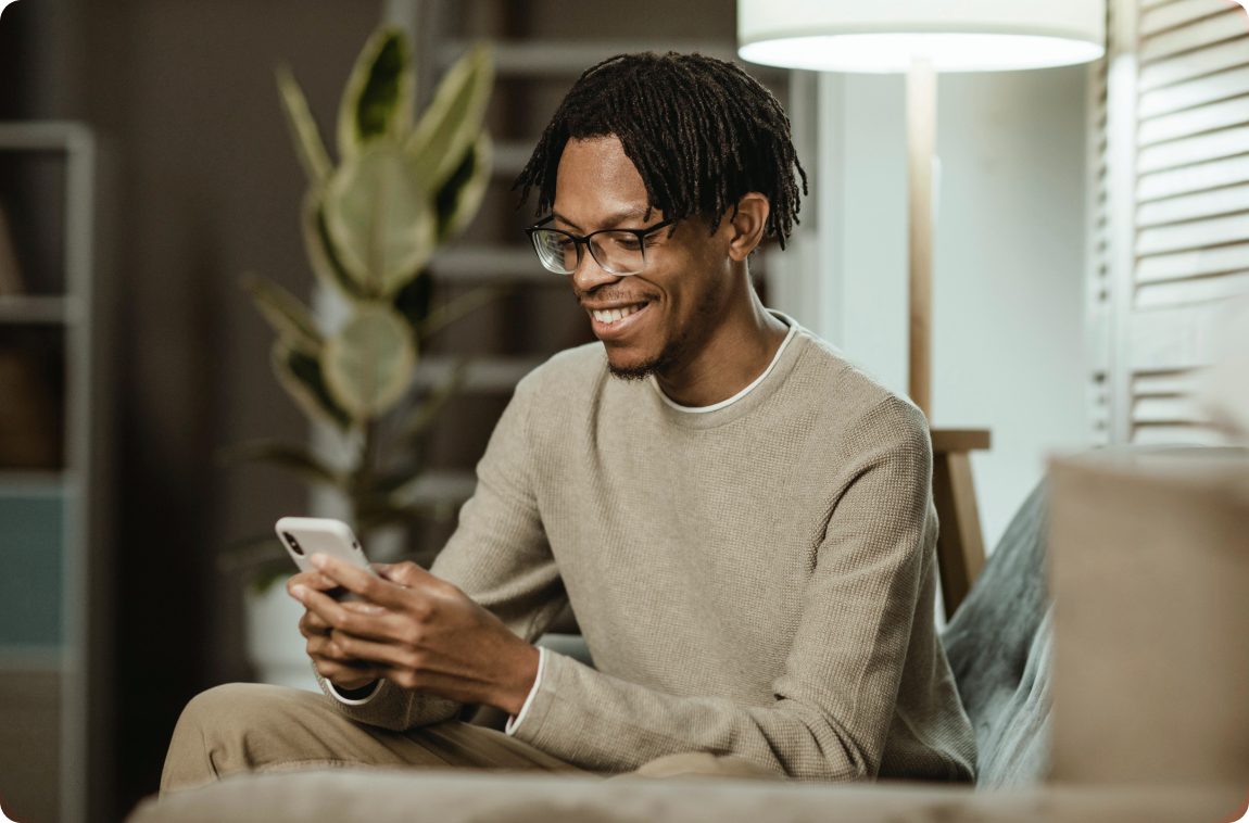 Homem negro com moletom bege usando smartphone moderno em casa no sofá